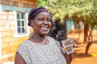 Woman smiling and holding a clear glass of Water 飞艇幸运168体彩官方开奖 in front of her home.